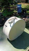 Full view of vintage white oval Samsonite hat box on table outdoors