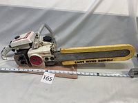 Full side view of 1967 Pioneer Holiday GT chainsaw showing white enamel body, red Pioneer logo, rigid handlebar, and 16 in. guide bar with 'Pioneer Chain Saws' marking.