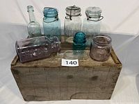 Full lot photo showing antique wooden crate with a variety of glass jars and bottles arranged on top, including some lying down.
