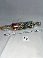 Full view of the antique glass rolling pin filled with colorful marbles next to measuring tape showing approximately 14 inches long.