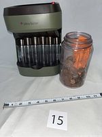 Full view of Ultra Sorter coin sorter with seven clear plastic coin tubes and an old Schram jar filled with assorted coins and wrappers beside it with a measuring tape and lot number card.