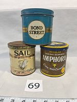 Front view of three vintage pipe tobacco tins: Bond Street (blue), Sail Natural Nautical (cream with ship illustration), Amphora Regular Douwe Egberts (brown/yellow).