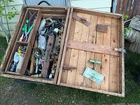 Photo of the open wooden tool chest showing an assortment of vintage hand tools and hardware inside compartments, plus a small 'NO BREAKFAST' sign attached to the lid.