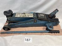 Full side view of blue hydraulic trolley jack on orange fabric with detachable handle separated