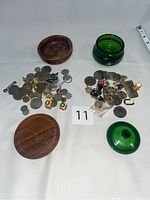 Wooden shaving soap jar and green glass jar with assorted men's knick knacks including coins, buttons, cuff links, dice, bottle opener, watch, money clip, bracelet, tie pin, miniature beer mug, and tin soldier figurine.