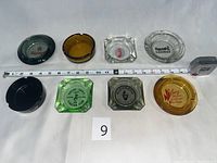 Eight vintage casino ashtrays of different colors and shapes laid out with a tape measure and numbered card for scale