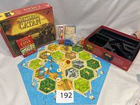 Settlers of Catan board game components including the hex tile board arranged, blue and orange pieces, resource cards, box and insert tray.