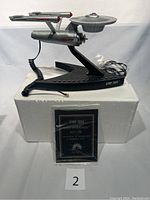 Photo of the Star Trek Enterprise phone handset and base on black stand, showing cables and certificate in front.