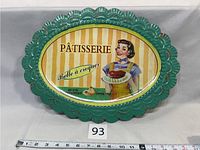 Oval vintage advertising tin tray with scalloped green edges and woman holding a pastry illustration on striped background.