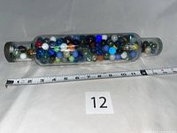 Full view of the vintage glass rolling pin filled with colorful assorted marbles, with measuring tape showing length approximately 14 inches.