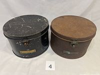 Photo of both WW2 military hat boxes, showing black box with wear and rusted patina box side by side