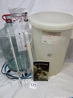Lot includes a 5 gallon glass carboy with a red handle lifter, a large white 5 gallon plastic fermentor with lid, clear plastic siphon labeled 'Siphon-Pacer', wine thief, stir spoon, bottle filler wand, blue warming coil, and a guide booklet.
