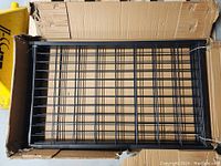 Top-down view of black welded wire panel of the kennel inside a cardboard box.