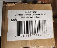 Close-up of product label on cardboard box showing item details: Boraam Torino Counter Stool, 24-Inch, Wire-Brush finish with barcode and item number 76724.
