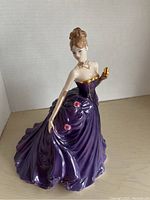 Front view of Lady Caroline figurine in purple gown with gold and pink flower accents and opera glasses in hand.