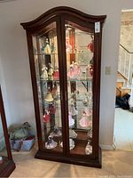 Front view of tall wood display cabinet with multiple glass shelves filled with collectible porcelain dolls.