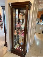Front view of tall dark-stained wood display cabinet with glass door closed, showing four glass shelves and mirrored back