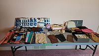 Full view of assorted ladies scarves, unopened pantyhose, gloves, purses, costume jewelry, sunglasses, and pen set arranged on a table