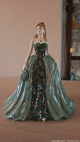 Front view of the Coalport porcelain figurine showing the emerald green gown detailed with gold floral patterns and the figure holding a fan and purse.