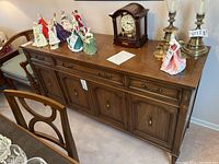 Front view showing wood buffet with three drawers and lower cabinet, with decorative porcelain figurines and clock on top.