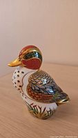 Front side of the Royal Crown Derby green winged mallard porcelain figurine showing red head, gold beak, and white body with black leaf patterns.