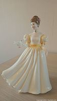Full side view of the Royal Doulton porcelain figurine 'Kathleen'. Shows the flowing pale yellow dress and the white bird on the right hand.