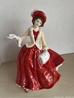 Front view showing the full figurine of the woman in red dress with fur-trimmed coat and matching muff and hat.