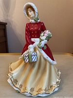 Front view of the Royal Doulton figurine showing red winter coat, bonnet, gift basket and bouquet details