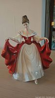 Front view of the Royal Doulton figurine showing the woman holding her red skirt with white bodice and floral details on shoulders.
