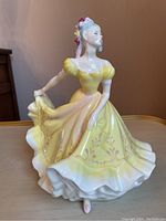 Front side view of the Royal Doulton Ninette figurine showing the detailed yellow dress with pink floral accents and the figure's face and upper body.