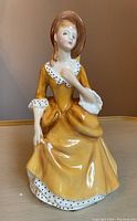 Front angle view of Royal Doulton Sandra figurine in yellow dress with bonnet hat, showing facial features and upper body details.