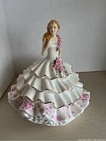 Front view of Royal Doulton Victoria porcelain figurine showing detailed white multi-layer ruffled gown with gold trim and pink floral accents.
