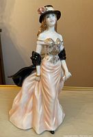 Front view of the porcelain figurine showing the woman in a detailed gown, black shawl, and hat with flower.