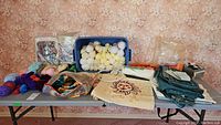 Full view of crafting supplies and yarn arranged on table including plastic bin with yarn, fabric remnants, and needlepoint canvas