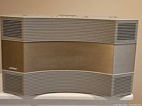 Front view of Bose AW-1 Acoustic Wave Music System showing beige front panel with white horizontal grille speaker covers and Bose logo on bottom left.