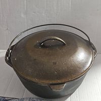 Cast iron kettle with lid and bail handle, front angle showing spout and handle.