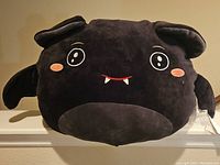 Front view of large black and dark gray Squishmallows plush depicting Emily the Bat with embroidered eyes, cheeks, and fangs, displayed upright.