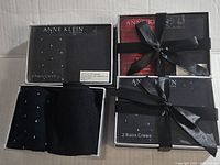 Top view of four Anne Klein boxes containing 8 pairs of crew socks, with some boxes tied with black ribbons and one box open showing black and blue patterned socks.
