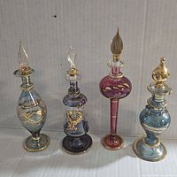 Four vintage Egyptian hand-painted glass perfume bottles with ornate stoppers and gold detailing, standing side by side.