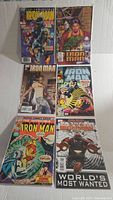 Photo showing 6 Iron Man comic books with various covers laid out flat.