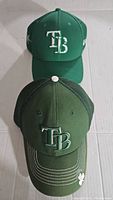 Two fitted Tampa Bay Rays caps stacked; green solid front cap and dark green mesh back cap