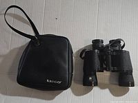 Black Tasco carrying case with wrist strap, placed next to Tasco binoculars