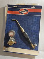 Torch handle mounted on original backing with attached pressure gauge regulator and brass torch head; packaging shows brand and product line.