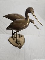 Front and side view of vintage brass cranes statue showing the two birds standing on an oval base with long necks and beaks.