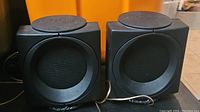 Pair of black cube-shaped Wharfedale Modus Cube speakers with visible branding and speaker grille.