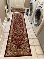 Long red floral runner carpet on tiled floor in narrow room with washer and dryer visible