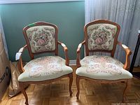Pair of matching wood frame armchairs with needlepoint upholstery showing dancing couple and floral designs