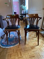 Pair of captain's chairs along a wooden parquet floor with rug and background furniture visible, showing the front and side of both chairs.