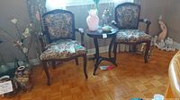Pair of wood framed chairs with floral fabric upholstery and some scratches, positioned on parquet floor with decorative items around.