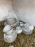 Full set of matching porcelain dishes on a kitchen counter, showing stacked plates, bowls, teacups with saucers, creamer, and sugar bowl.